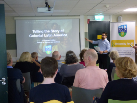 A class of people of different ages, genders and races, watching a presentation on Latin America