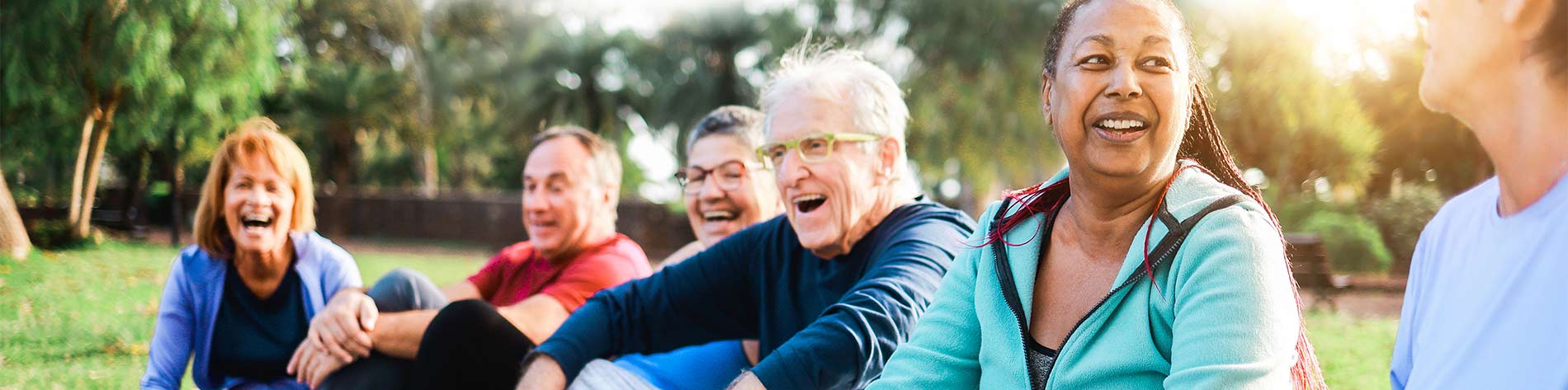 Group of people sitting in a park, laughing and taking part in exercise.